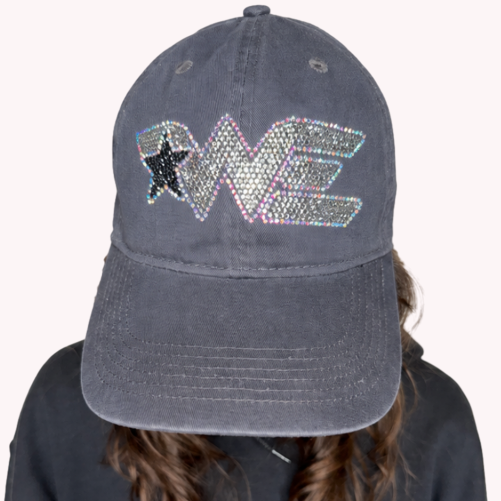 Dark gray distressed baseball cap with a sparkly rhinestone logo on the front, worn by a person in a dark hoodie.